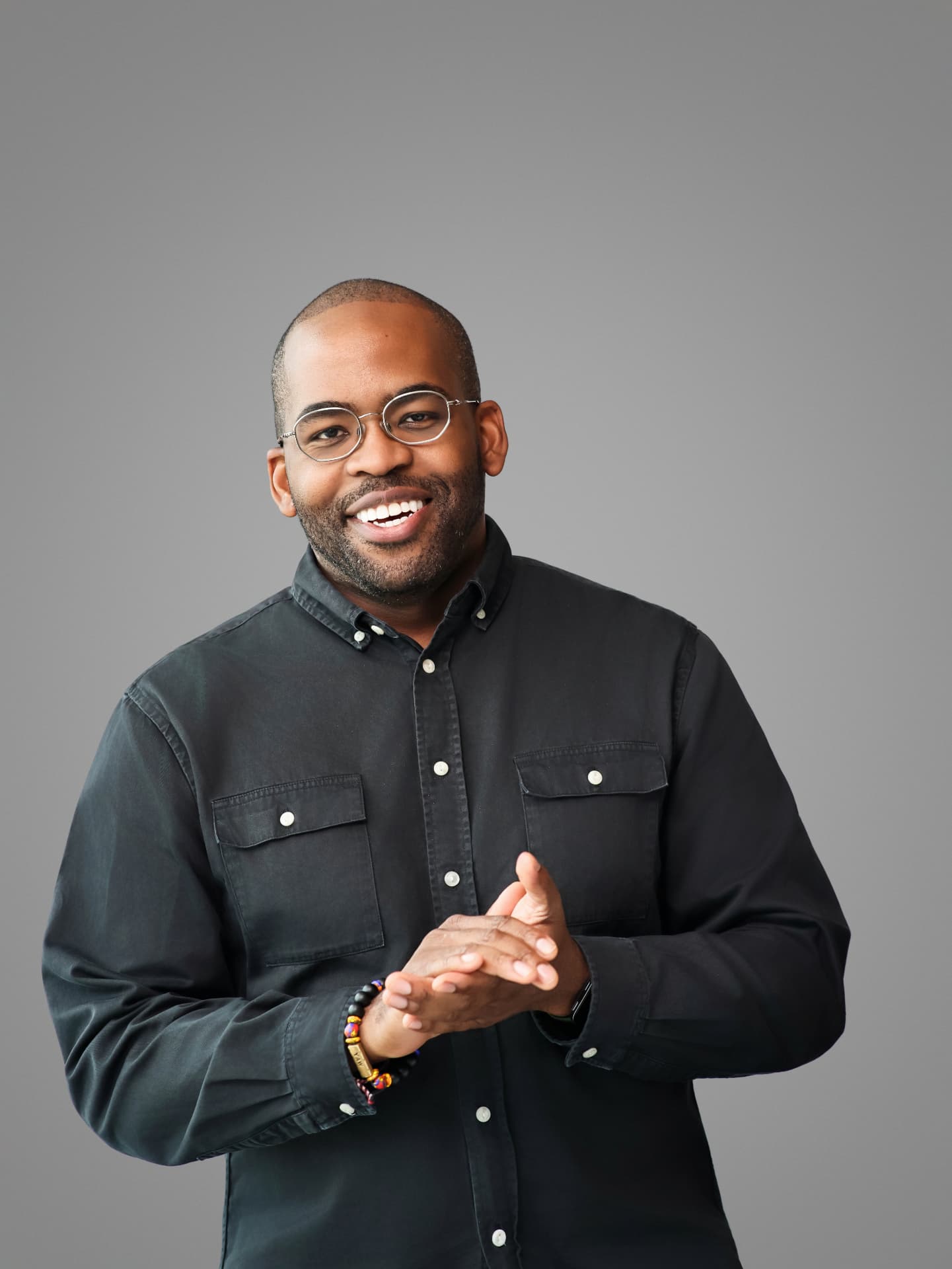 Smiling man in glasses and a black button-up shirt on a gray backdrop