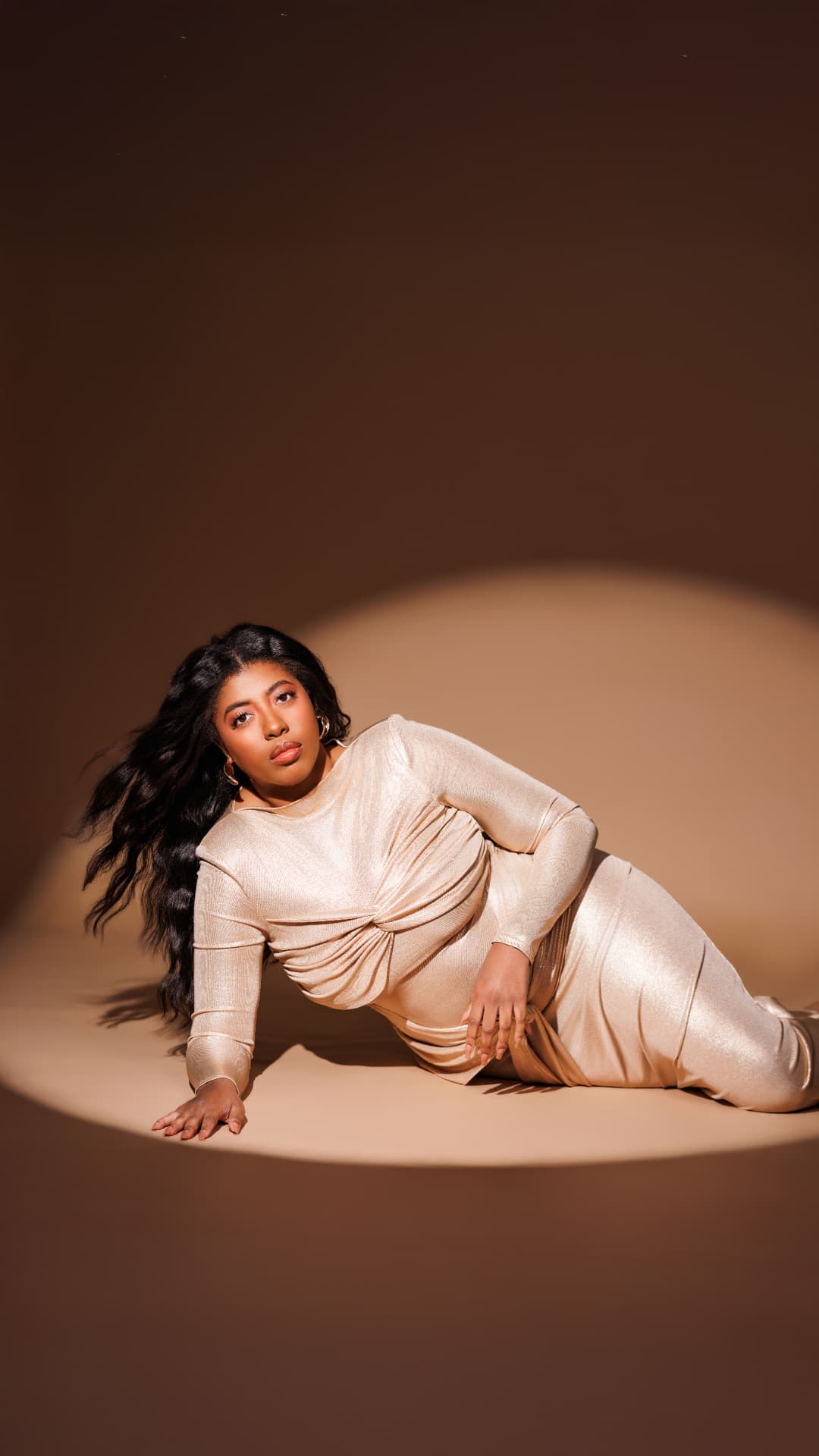 Client reclining in a champagne dress under a warm spotlight