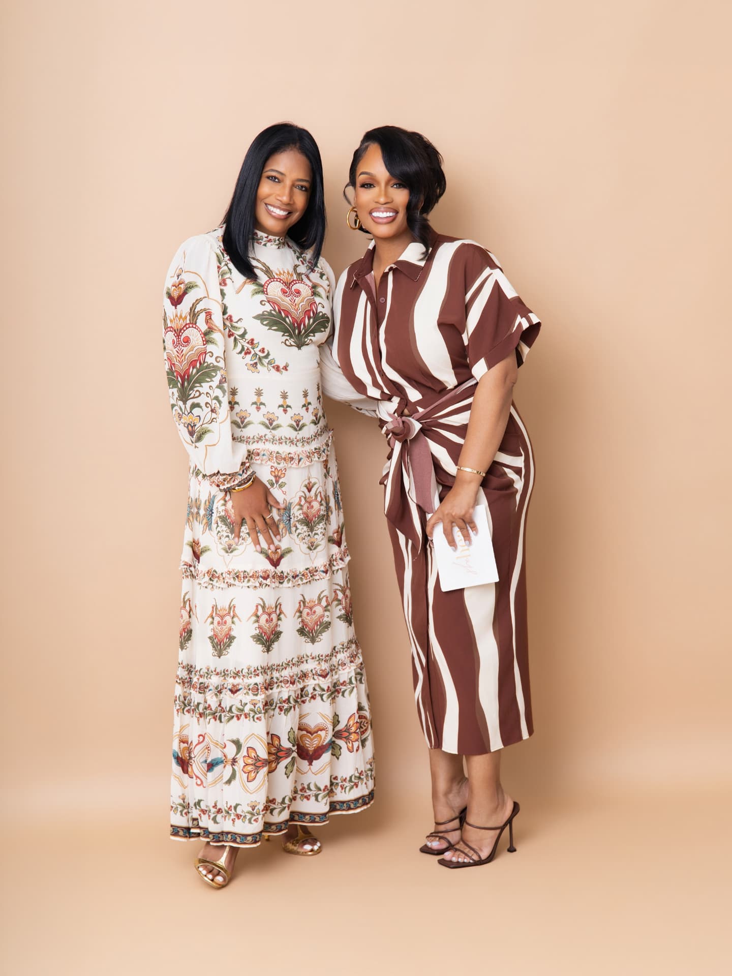 Two podcast hosts posing together on a tan backdrop