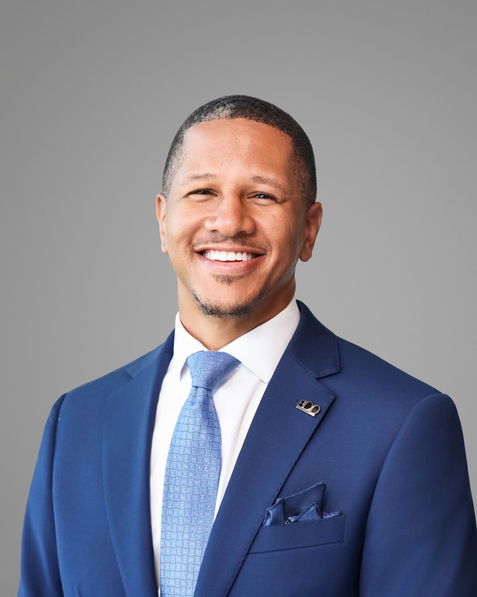 Smiling man in a navy suit and light blue tie on a gray backdrop