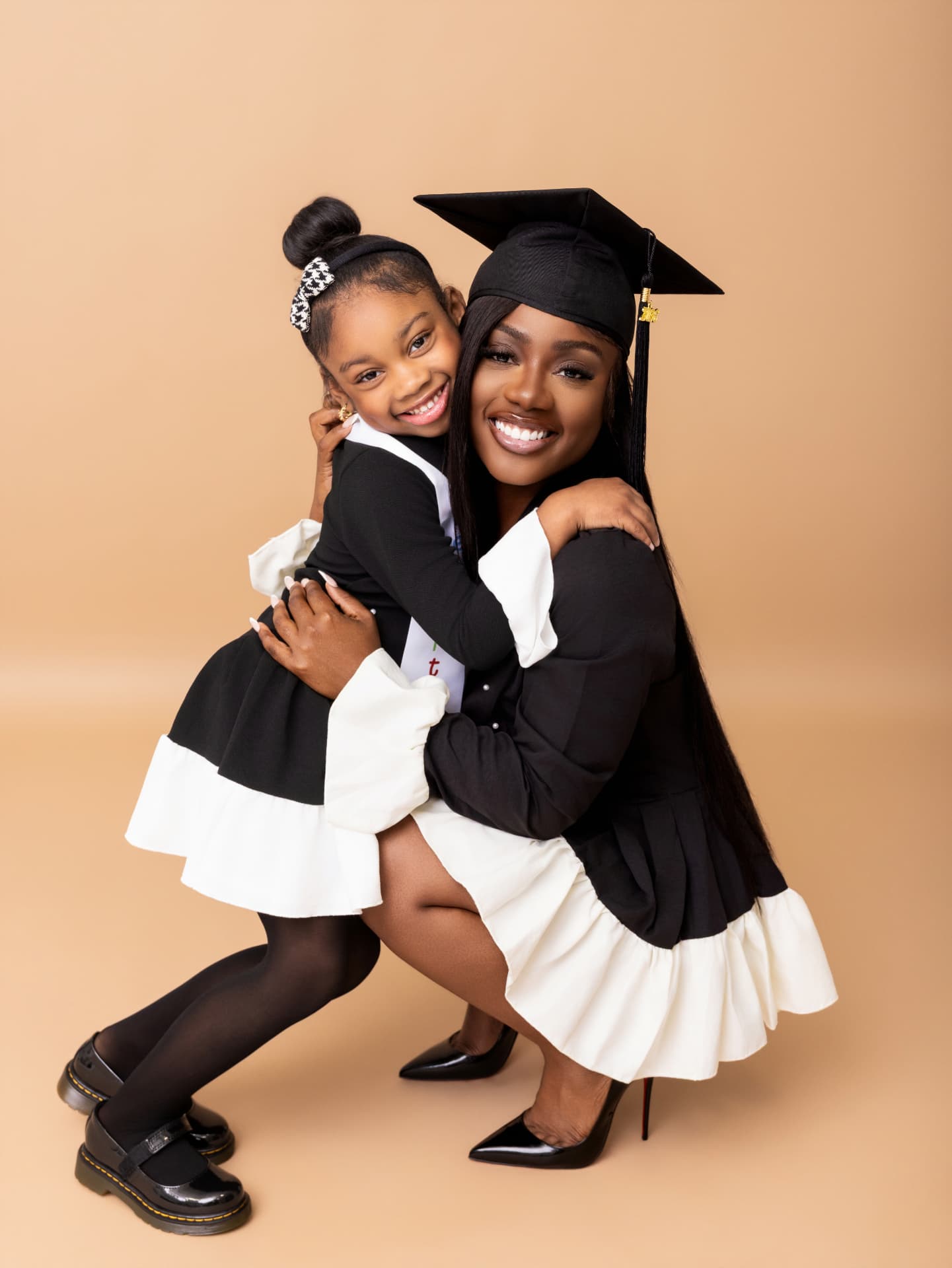 Graduate in a black cap hugging a young girl in a matching black and white outfit