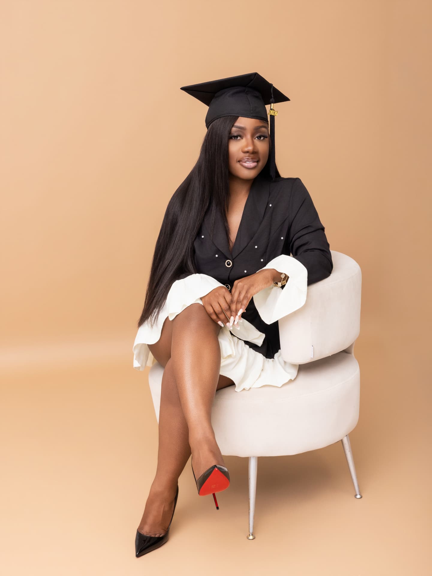 Graduate in a black cap seated on a white studio chair