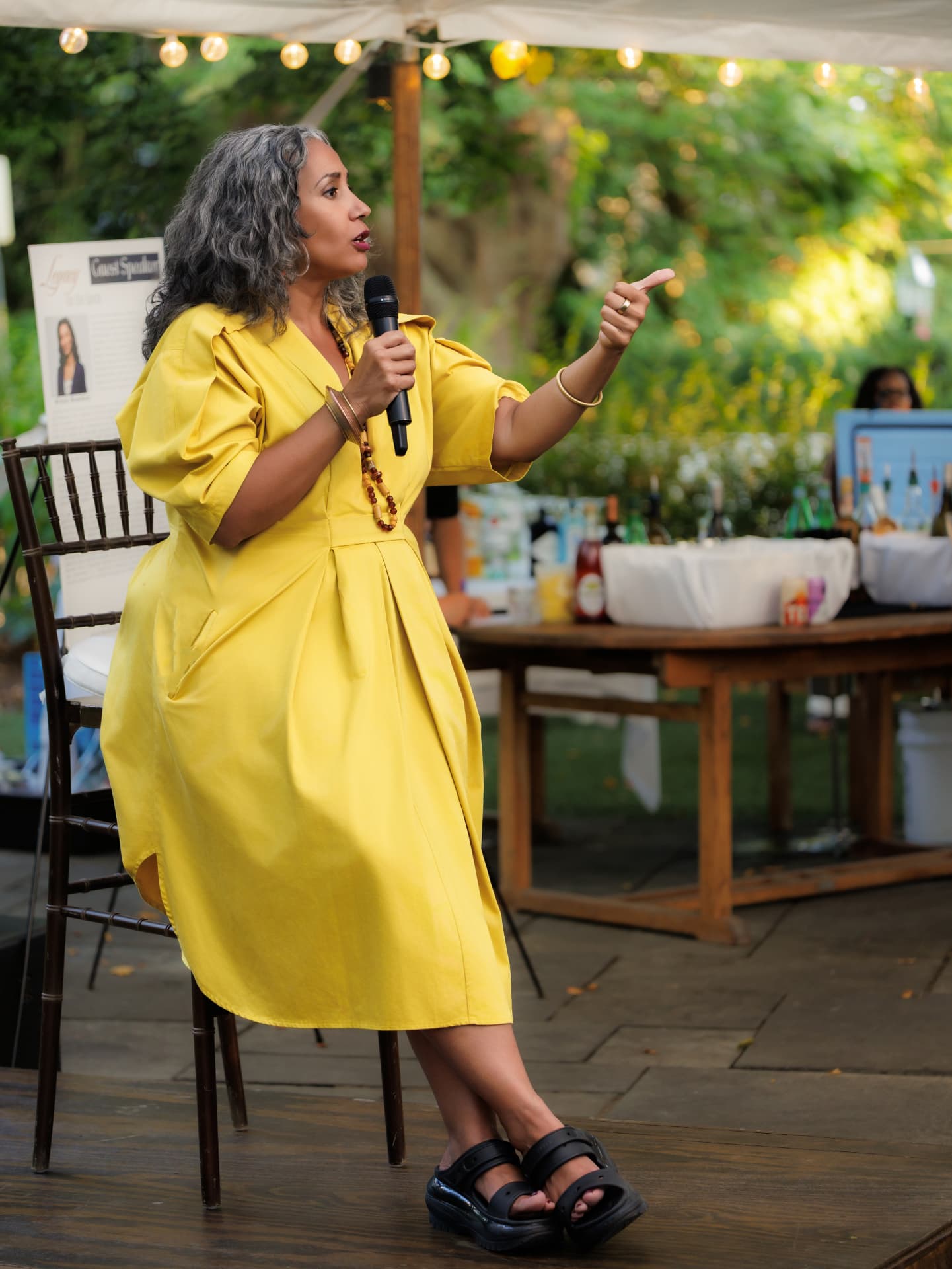 Guest speaker in a yellow dress talking into a microphone at an outdoor evening event