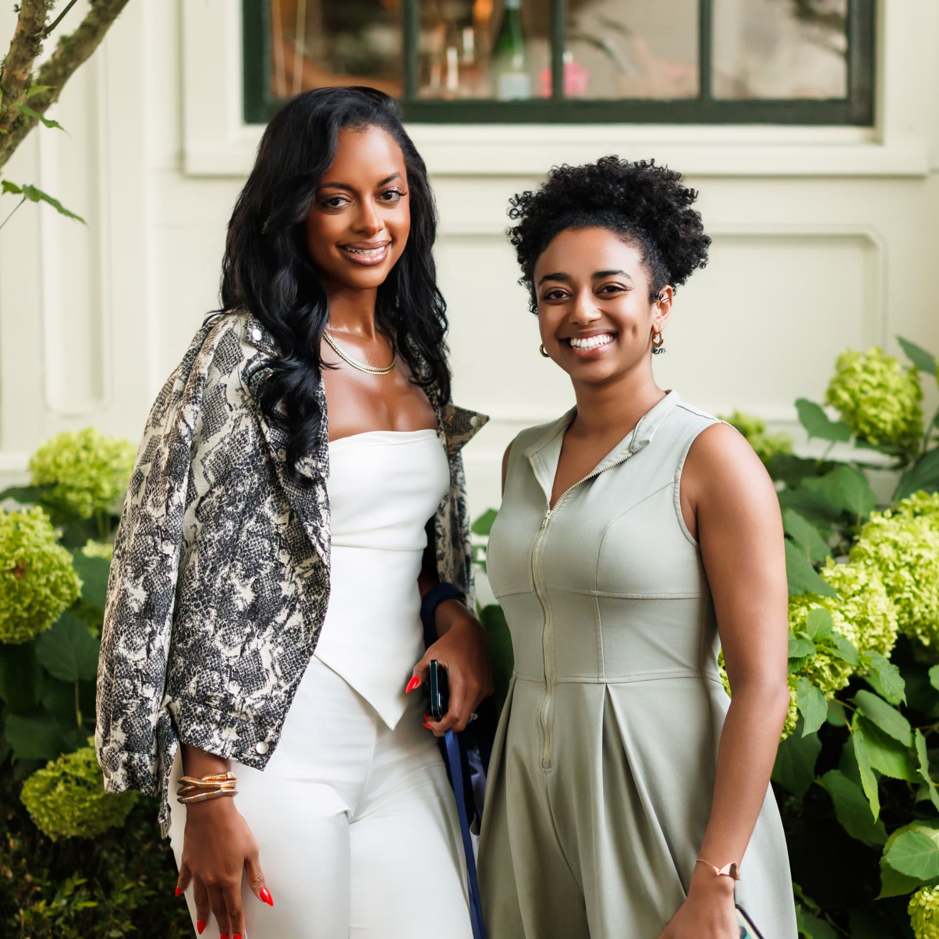 Two smiling guests posing together beside hydrangeas at an event
