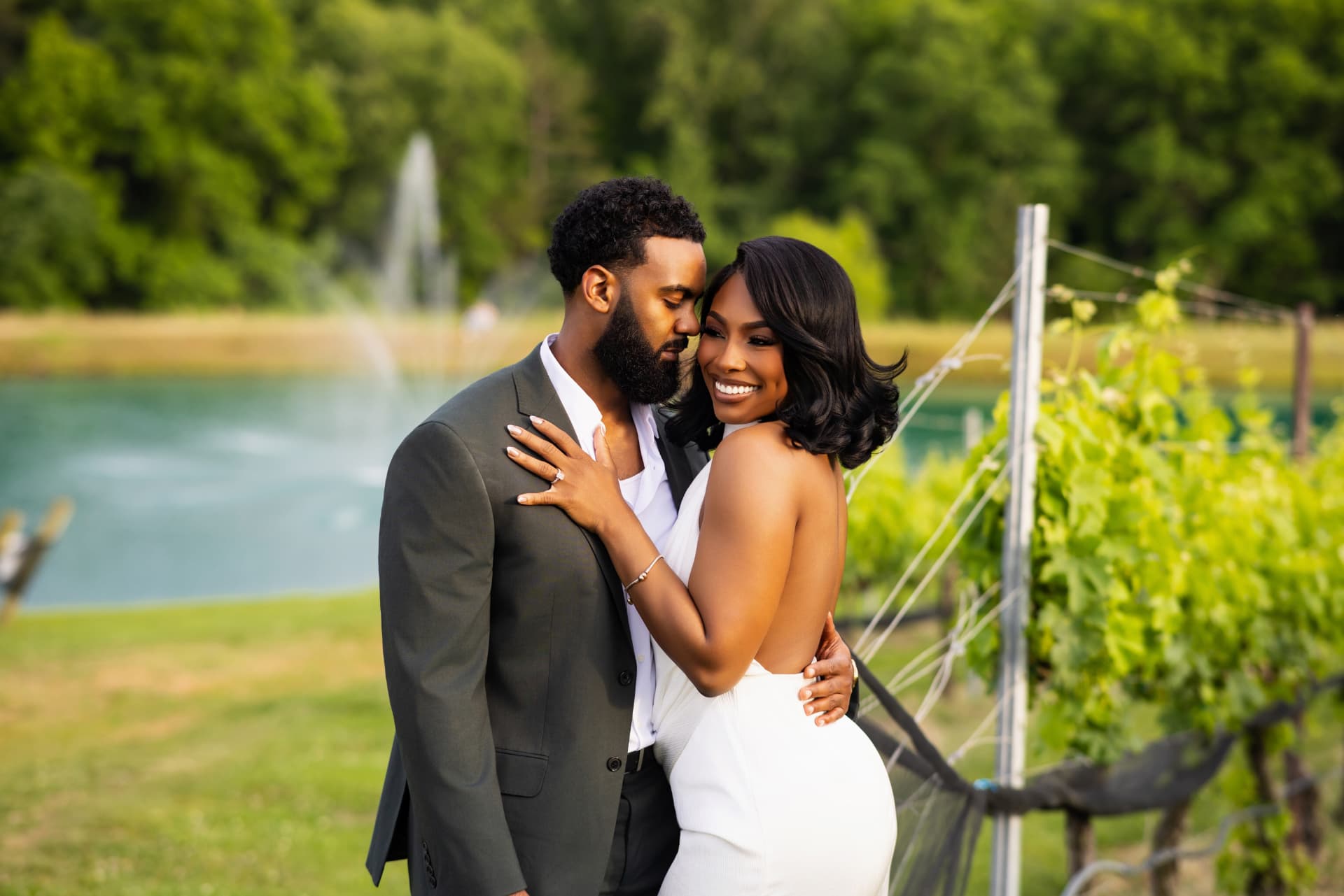 Engaged couple embracing beside a vineyard with a fountain behind them