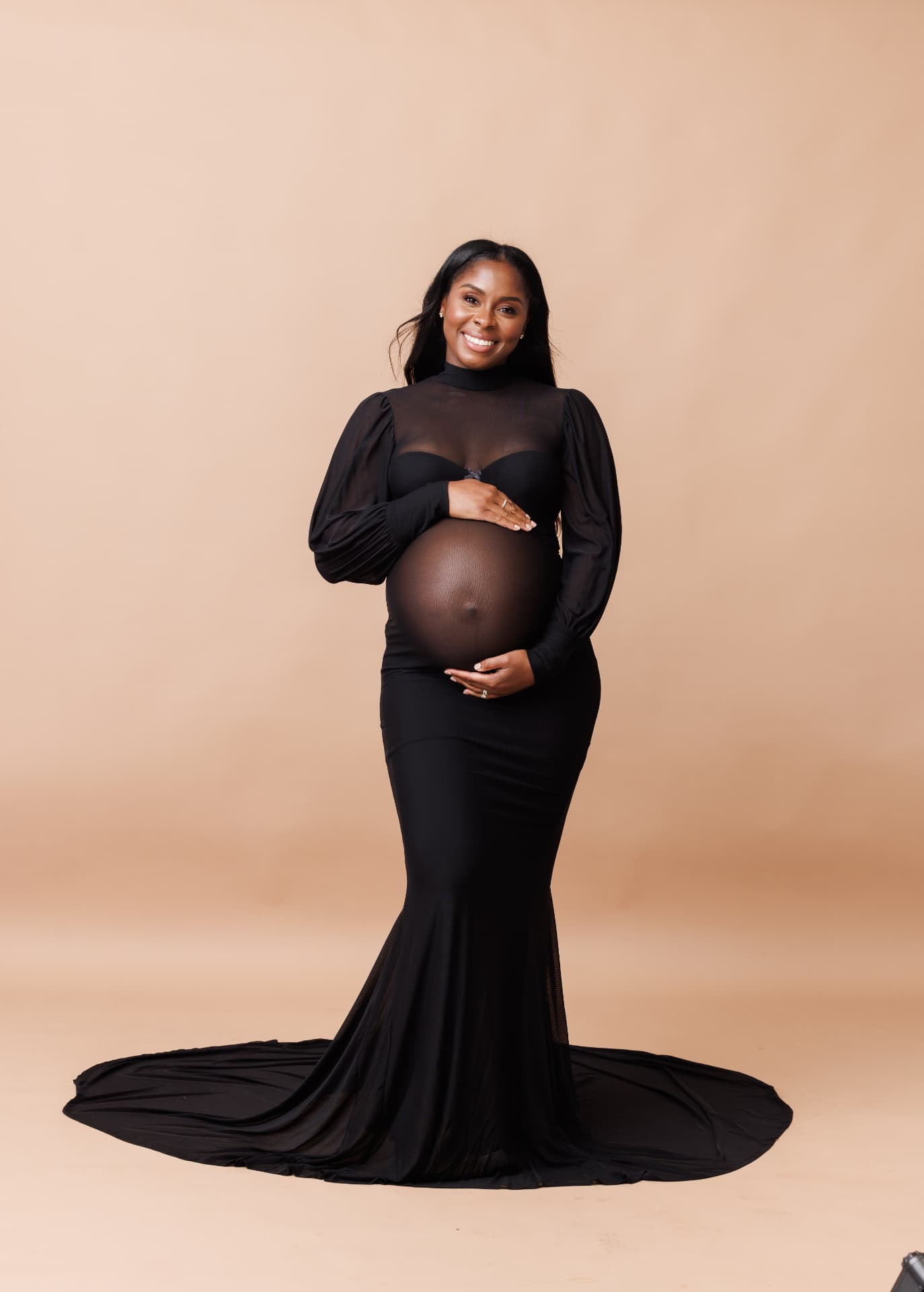 Expectant mother in a flowing black gown on a warm tan studio backdrop