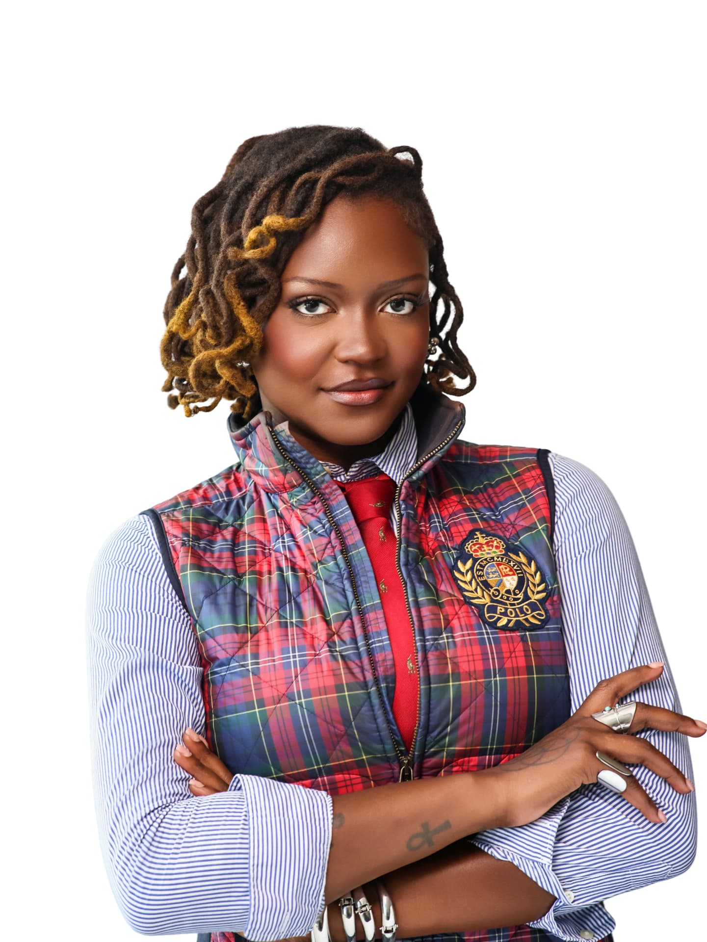 Woman with locs in a plaid vest and red tie, arms crossed on a white backdrop