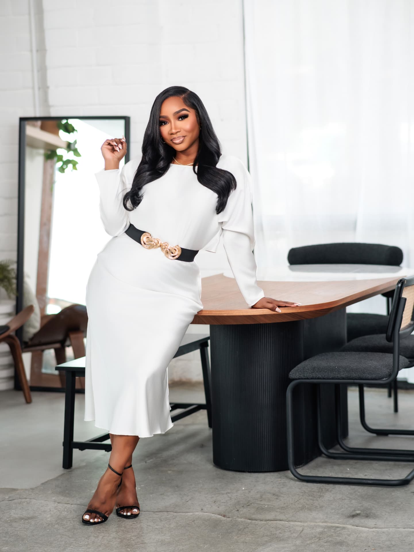 Client in a white dress seated on the edge of a wooden table in a bright loft