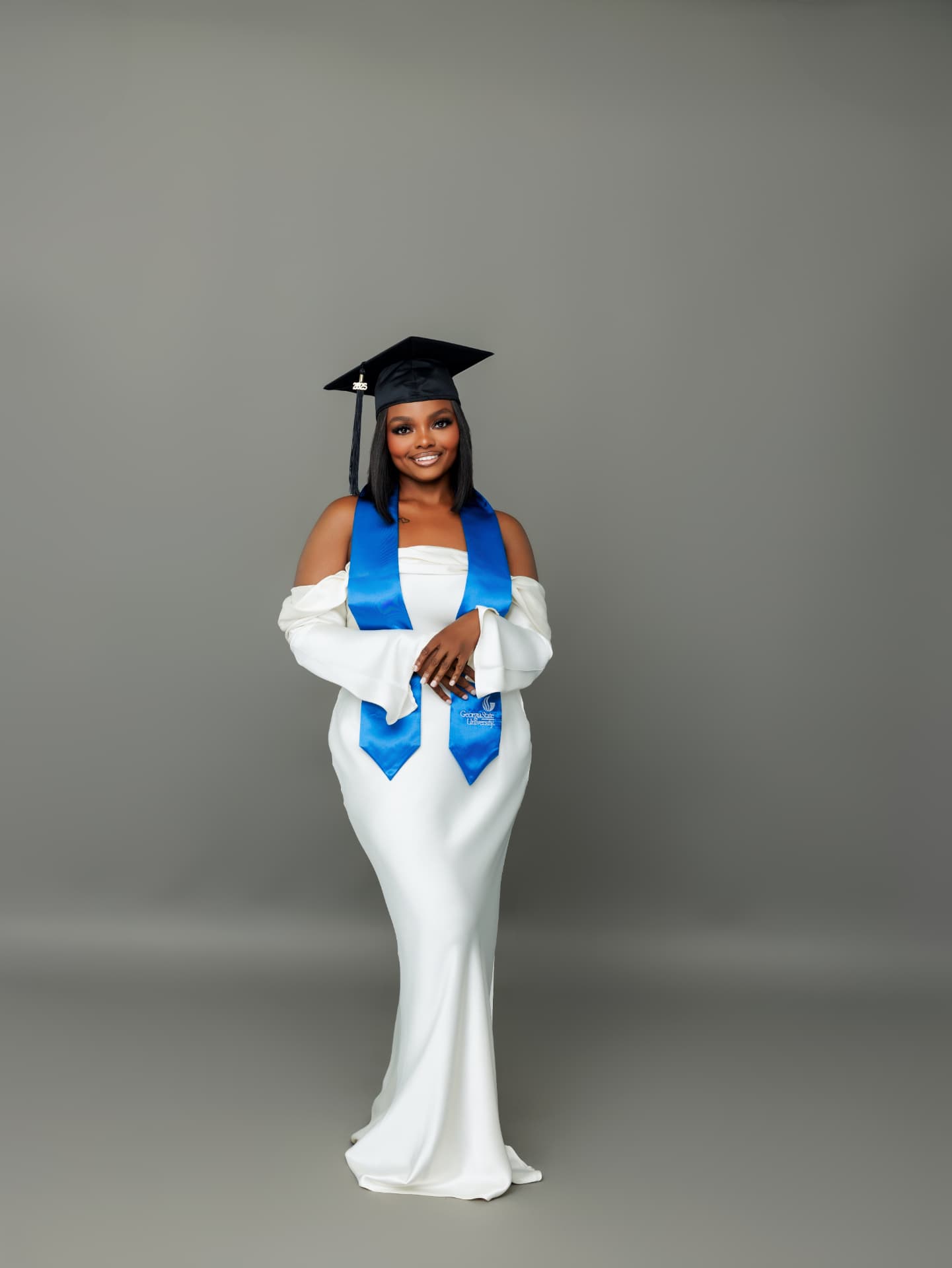 Graduate in a white satin gown, cap and blue stole