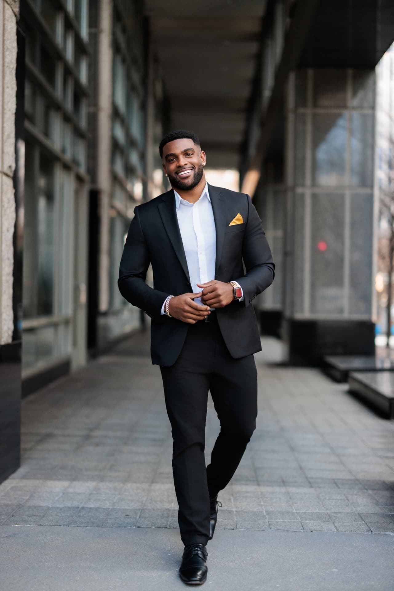 Client in a black suit walking and smiling along a city sidewalk